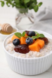 Photo of Delicious barley porridge with blueberries, pumpkin, dates and mint in bowl on white table, closeup