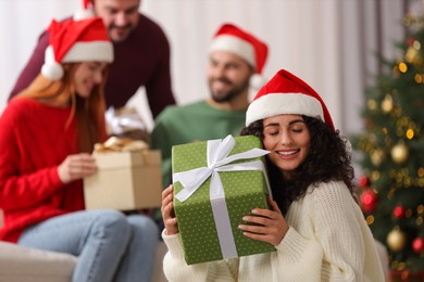 Photo of Christmas celebration in circle of friends. Happy young woman with gift box at home, selective focus