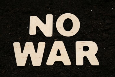 Photo of Words No War made of wooden letters on soil, top view