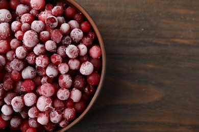 Photo of Frozen red cranberries in bowl on wooden table, top view. Space for text