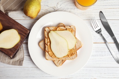 Photo of Slice of bread with peanut butter and pear on white wooden table, flat lay