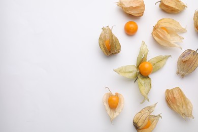 Ripe physalis fruits with calyxes on white background, flat lay. Space for text