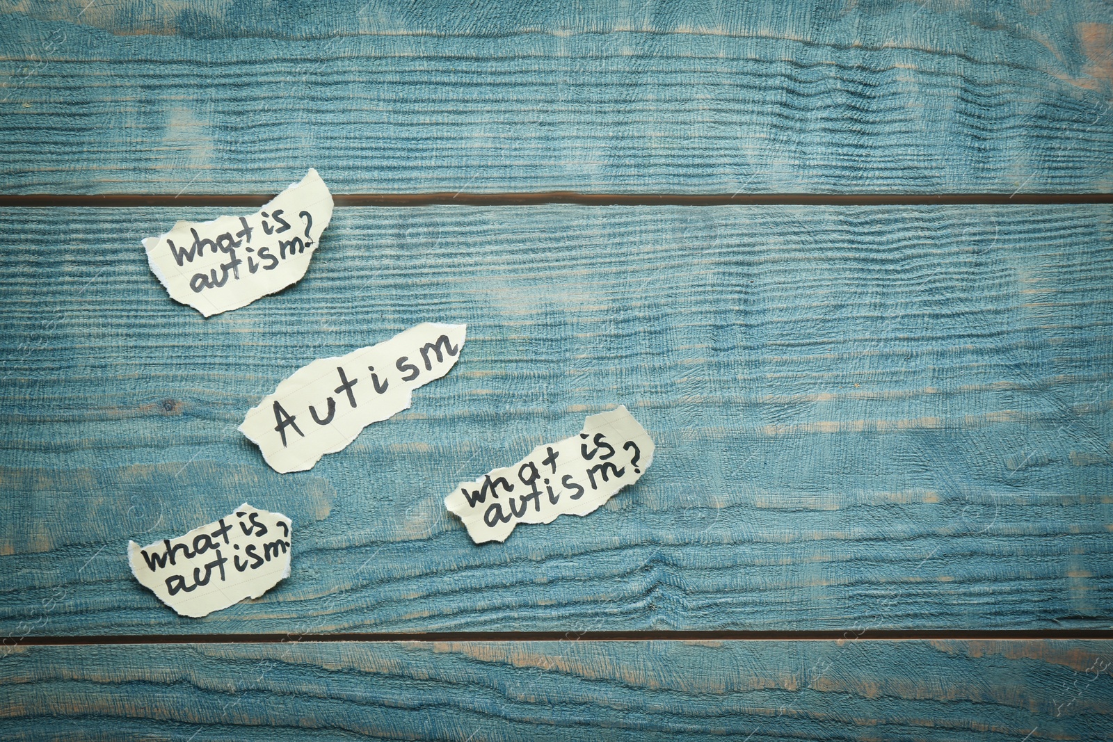 Photo of Paper pieces with phrases about autism on wooden background