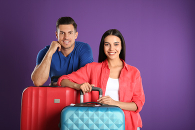 Photo of Happy couple with suitcases for summer trip on purple background. Vacation travel