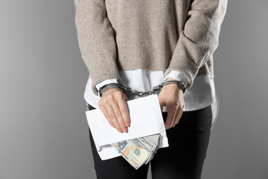 Photo of Woman in handcuffs holding bribe money on grey background, closeup