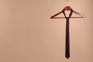 Photo of Hanger with silk tie on light brown background. Space for text