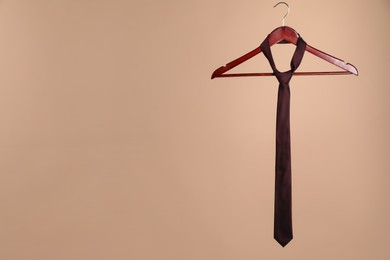 Hanger with silk tie on light brown background. Space for text