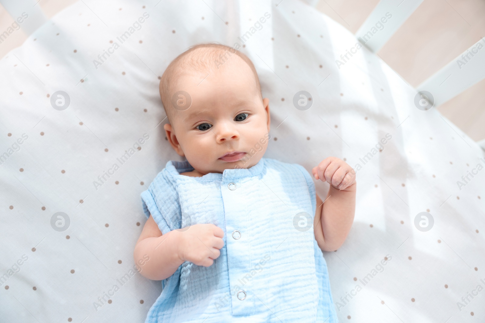 Photo of Cute little baby lying in crib at home, top view