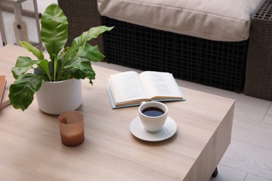 Photo of Coffee, candle, book and houseplant on wooden table indoors