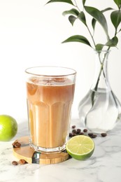 Photo of Refreshing iced coffee with milk in glass, beans and fresh limes on white marble table