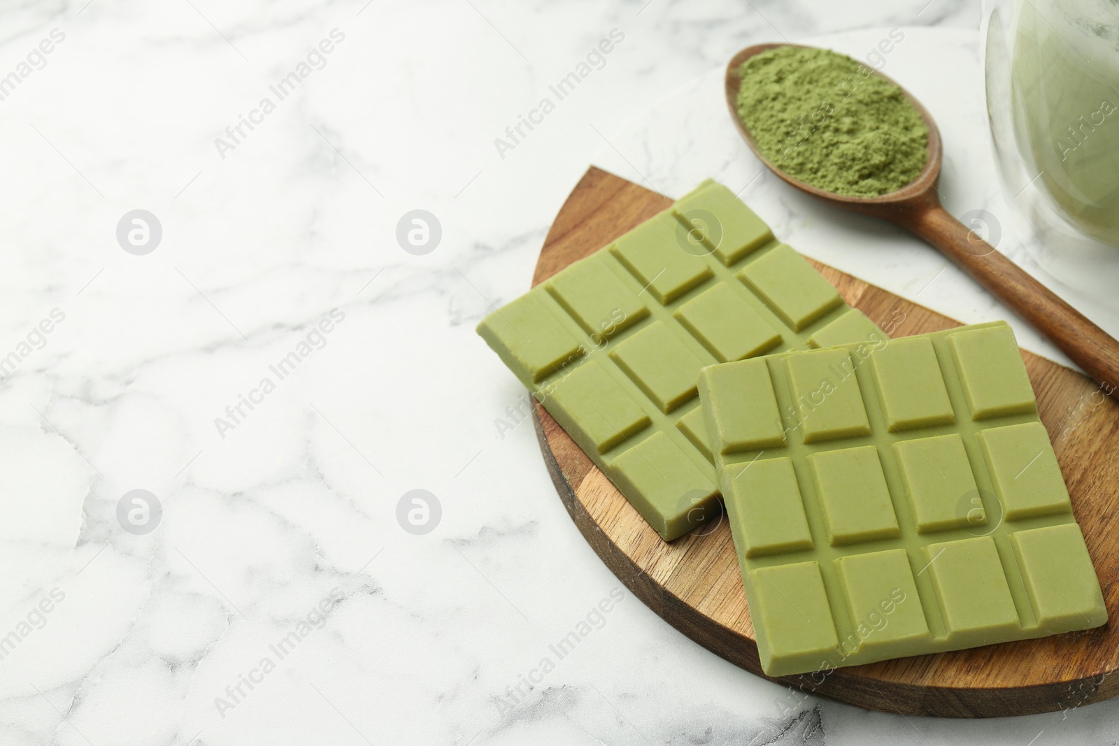 Photo of Pieces of tasty matcha chocolate bar and powder in spoon on white marble table, closeup. Space for text