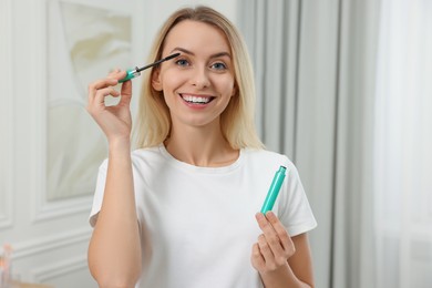 Photo of Beautiful happy woman applying mascara at home