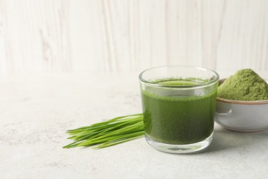 Photo of Wheat grass drink in glass, fresh sprouts and bowl of green powder on light table. Space for text