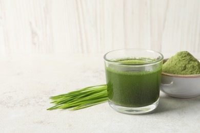 Wheat grass drink in glass, fresh sprouts and bowl of green powder on light table. Space for text