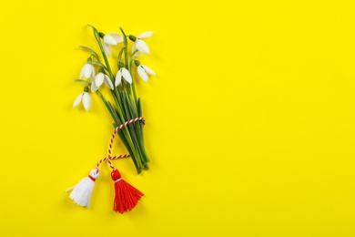 Photo of Beautiful snowdrops with traditional martisor on yellow background, flat lay and space for text. Symbol of first spring day