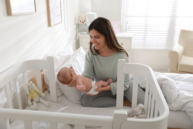 Photo of Happy young mother with her cute newborn baby near bedside crib at home