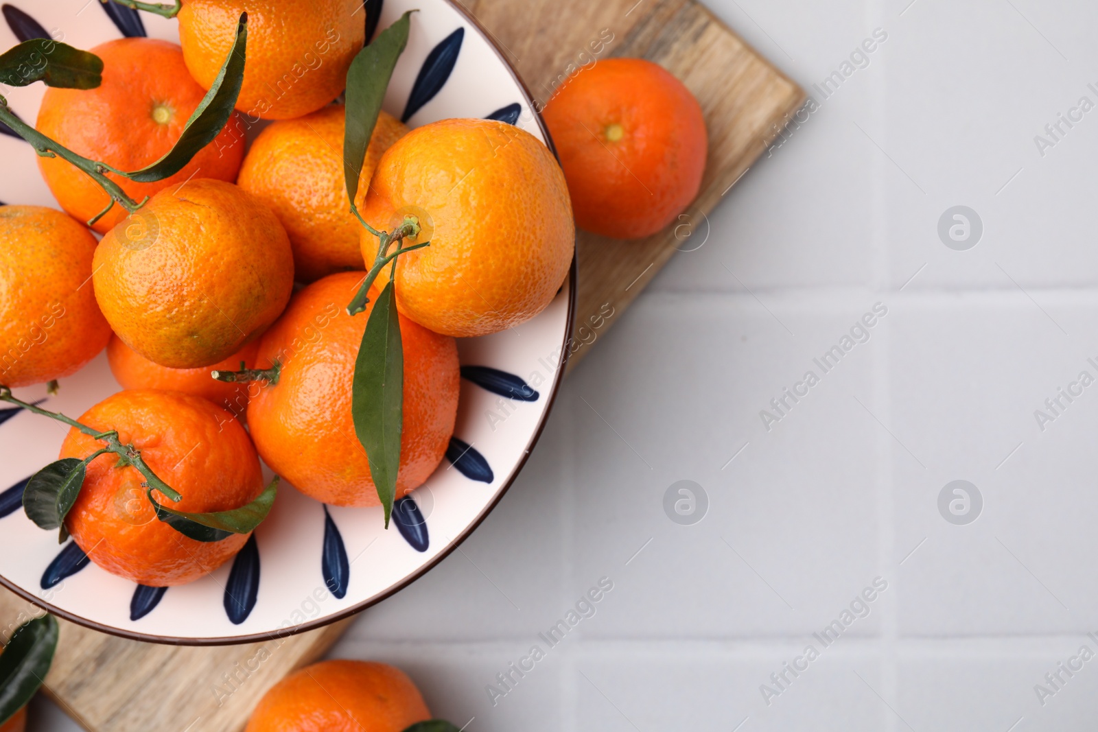 Photo of Fresh ripe tangerines with green leaves on white tiled table, top view. Space for text