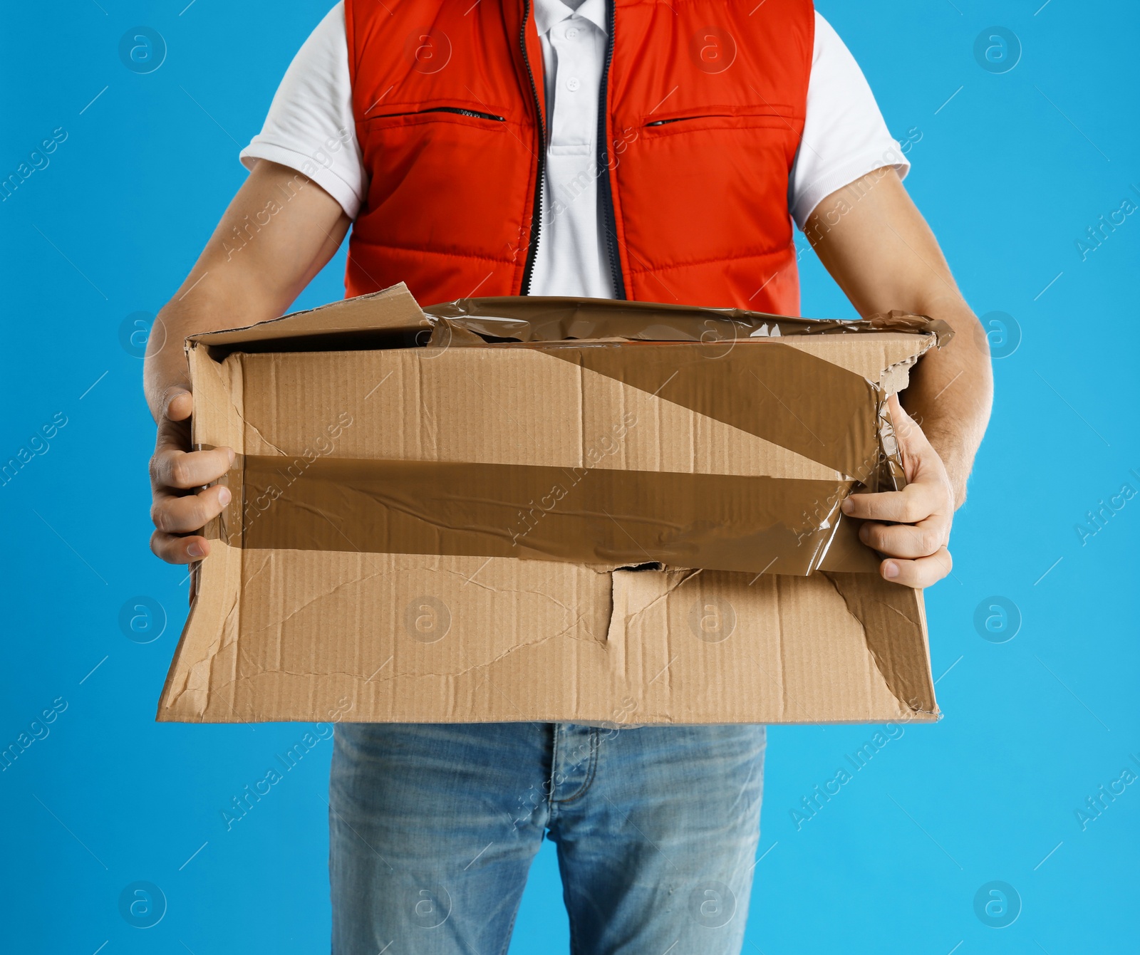 Photo of Courier with damaged cardboard box on blue background, closeup. Poor quality delivery service