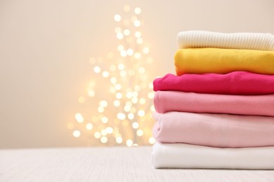 Photo of Stack of folded clothes on wooden table against beige background with blurred lights, space for text