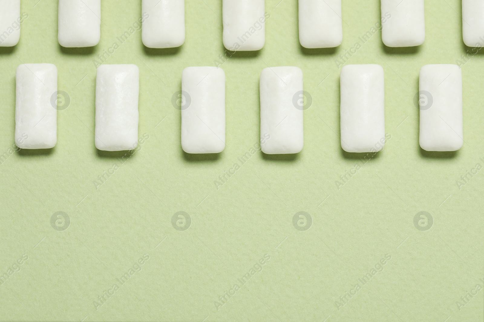 Photo of Tasty white chewing gums on light green background, flat lay. Space for text