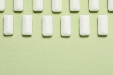 Photo of Tasty white chewing gums on light green background, flat lay. Space for text