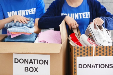 Female volunteers collecting clothes and shoes into donation boxes indoors