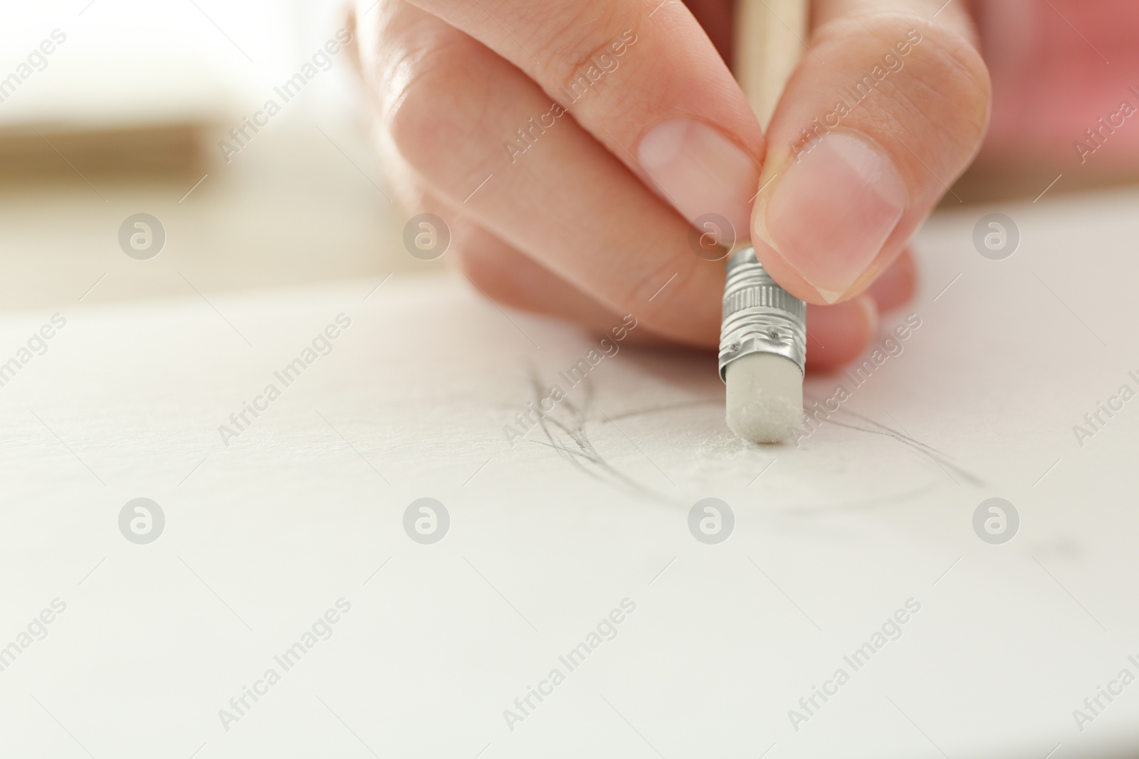 Photo of Woman correcting picture in notepad with pencil eraser, closeup