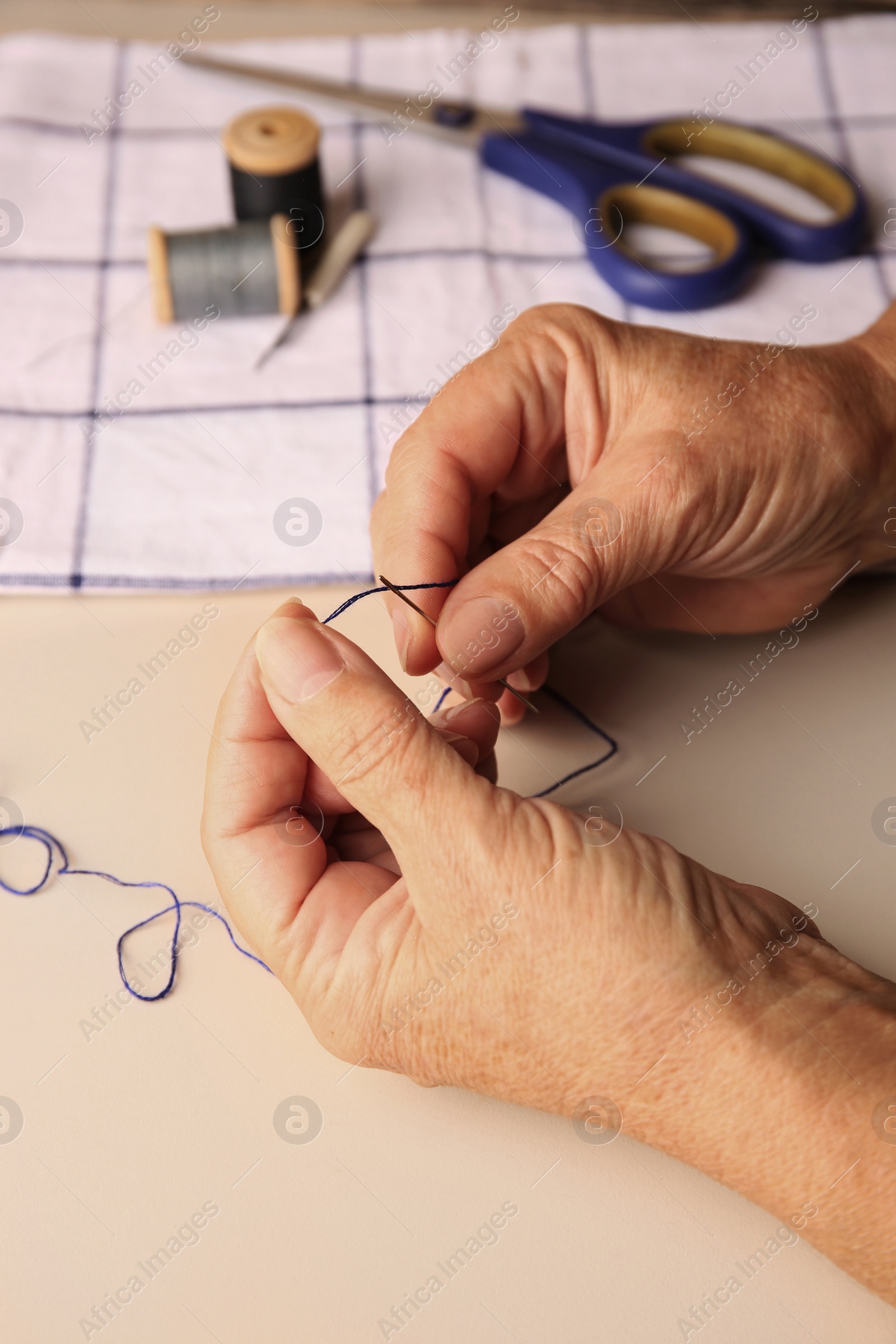 Photo of Closeup view of woman threading needle at beige table