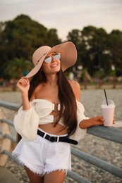 Beautiful young woman with tasty milk shake outdoors