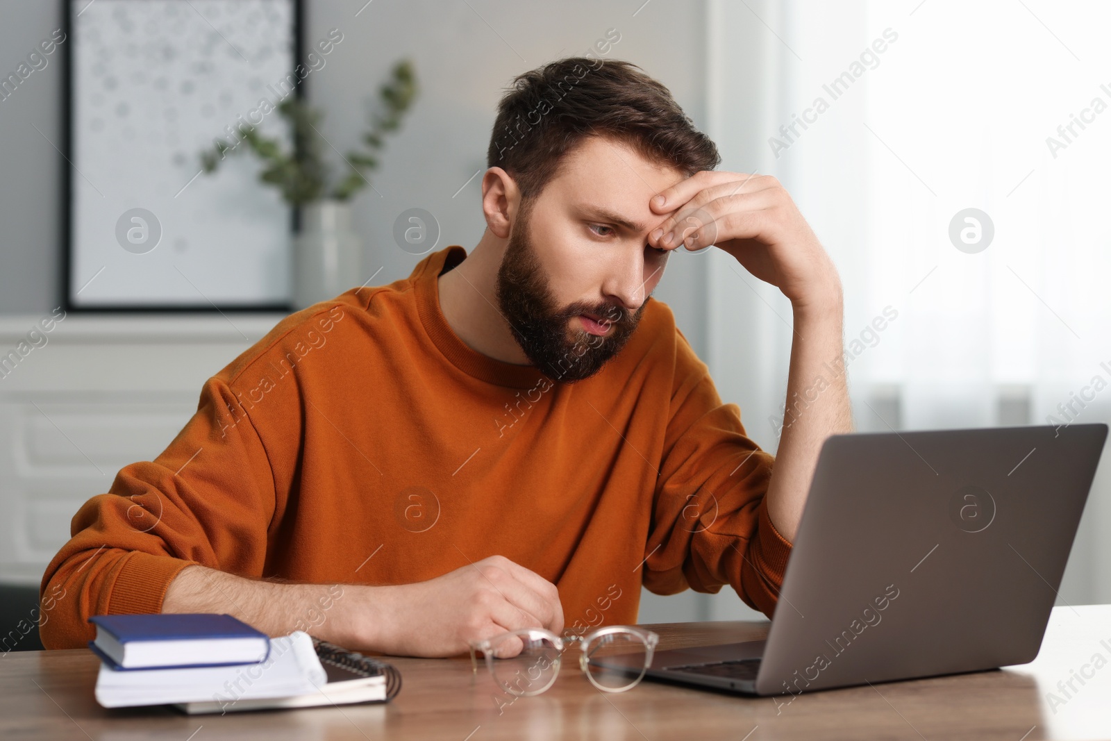 Photo of Overwhelmed man sitting with laptop at table indoors