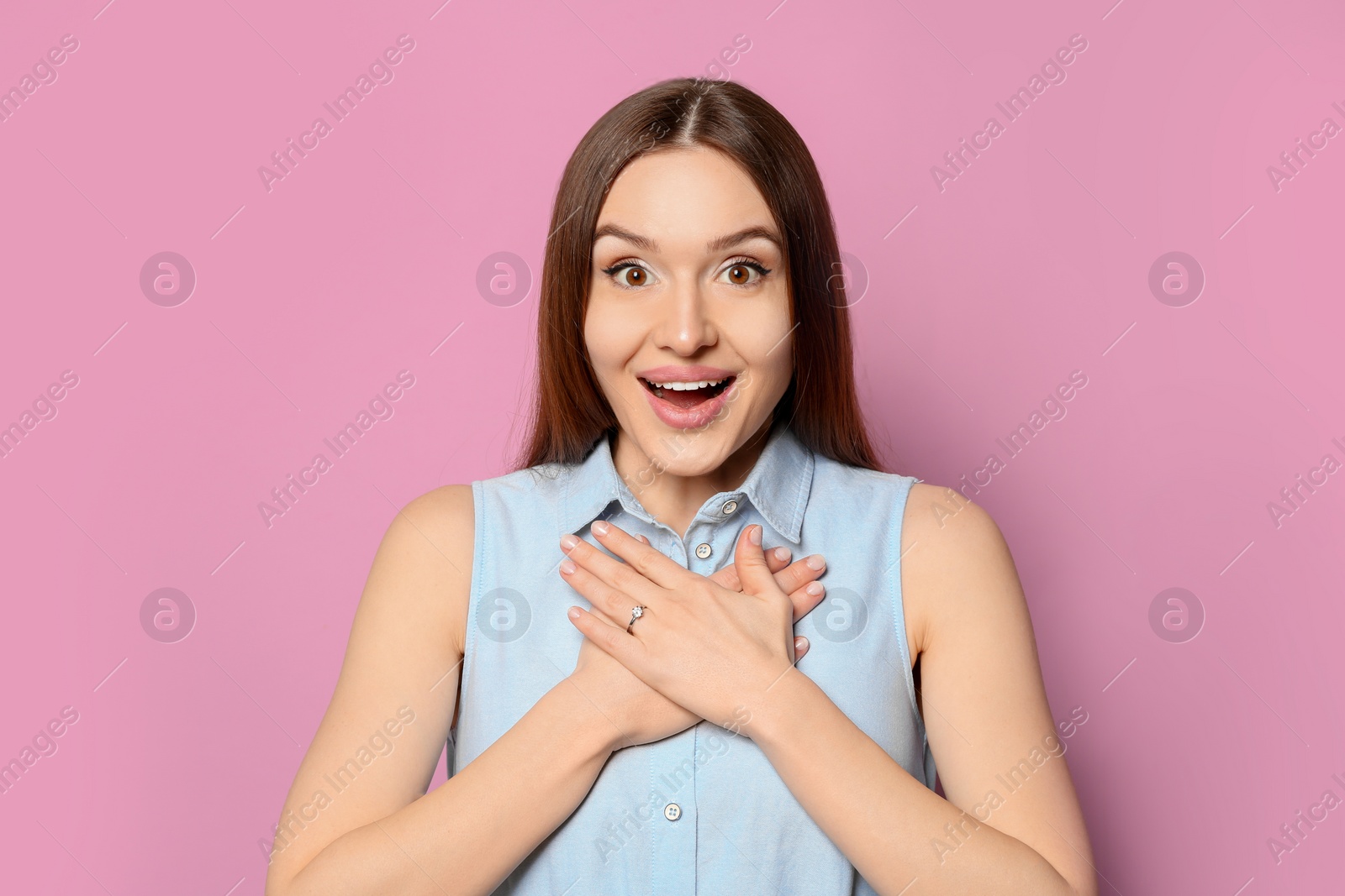 Photo of Emotional young woman wearing beautiful engagement ring on pink background
