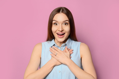 Photo of Emotional young woman wearing beautiful engagement ring on pink background