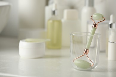 Photo of Natural face roller, gua sha tool and cosmetic products on counter in bathroom. Space for text