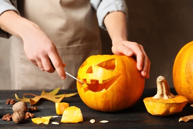 Photo of Woman making Halloween pumpkin head jack lantern on wooden table, closeup