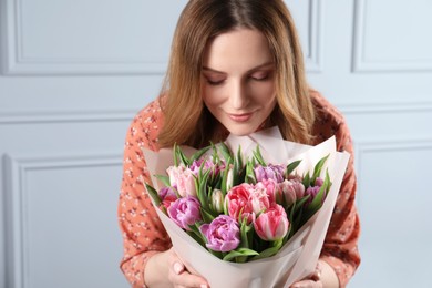 Photo of Happy young woman with bouquet of beautiful tulips indoors