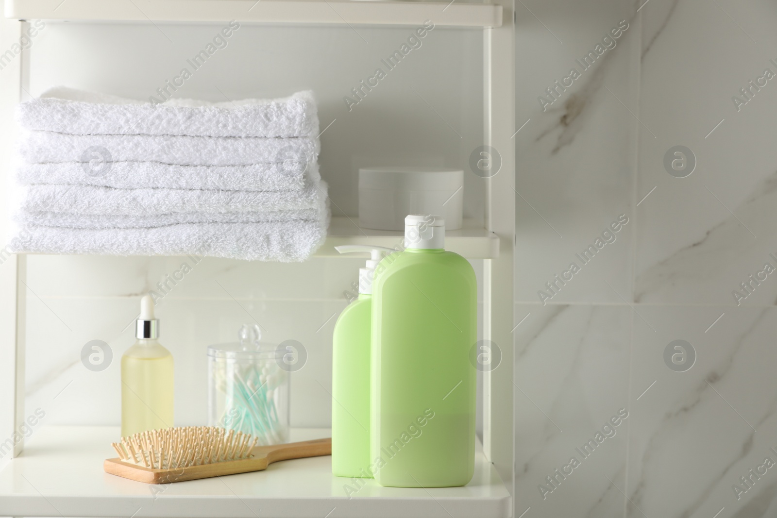 Photo of Stack of towels, hairbrush, shampoo and other toiletries on shelves near white marble wall