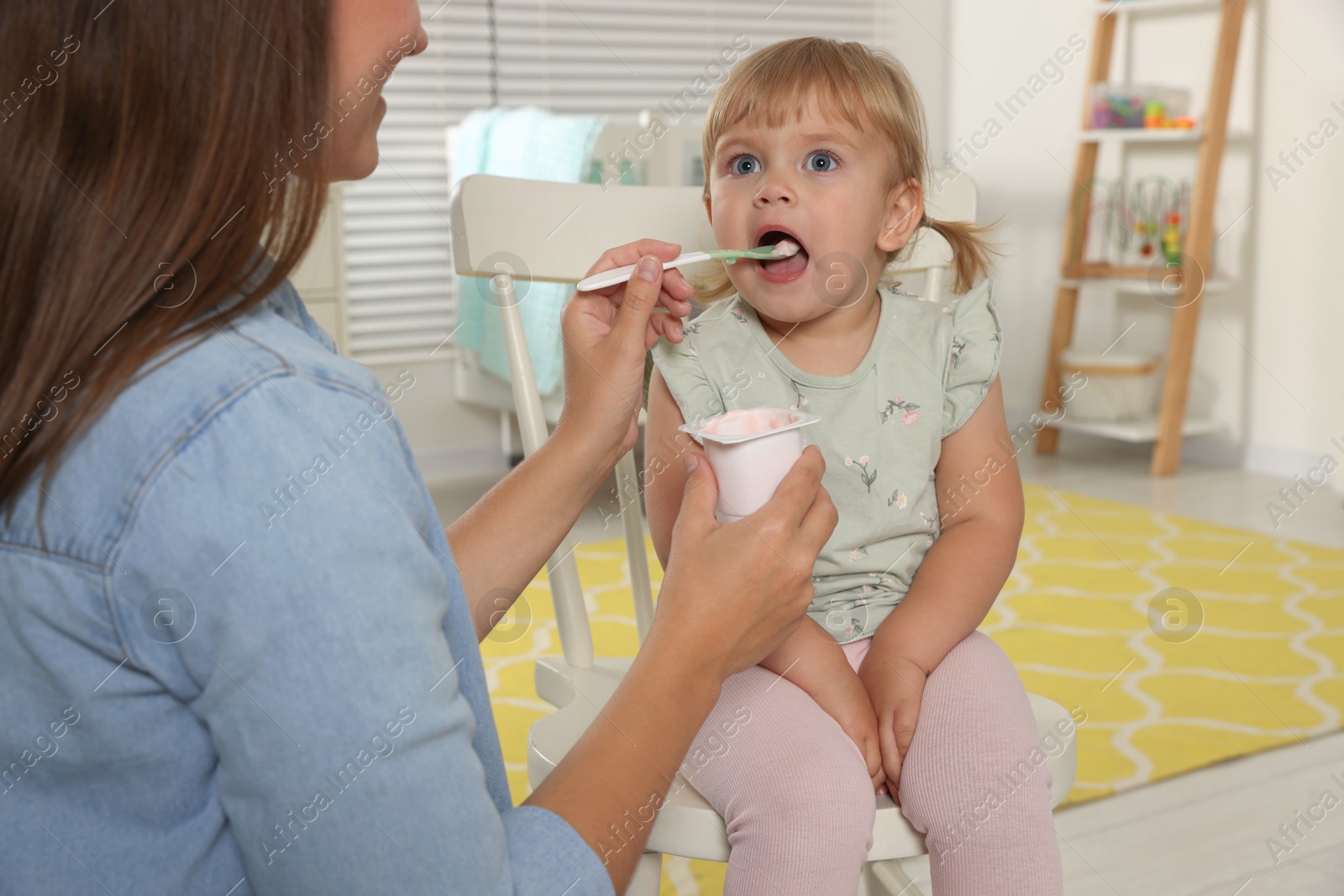 Photo of Mother feeding her cute little child with yogurt at home