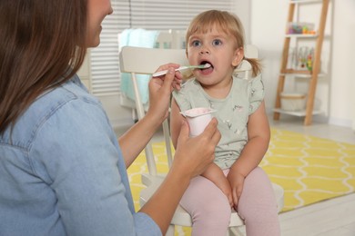 Mother feeding her cute little child with yogurt at home