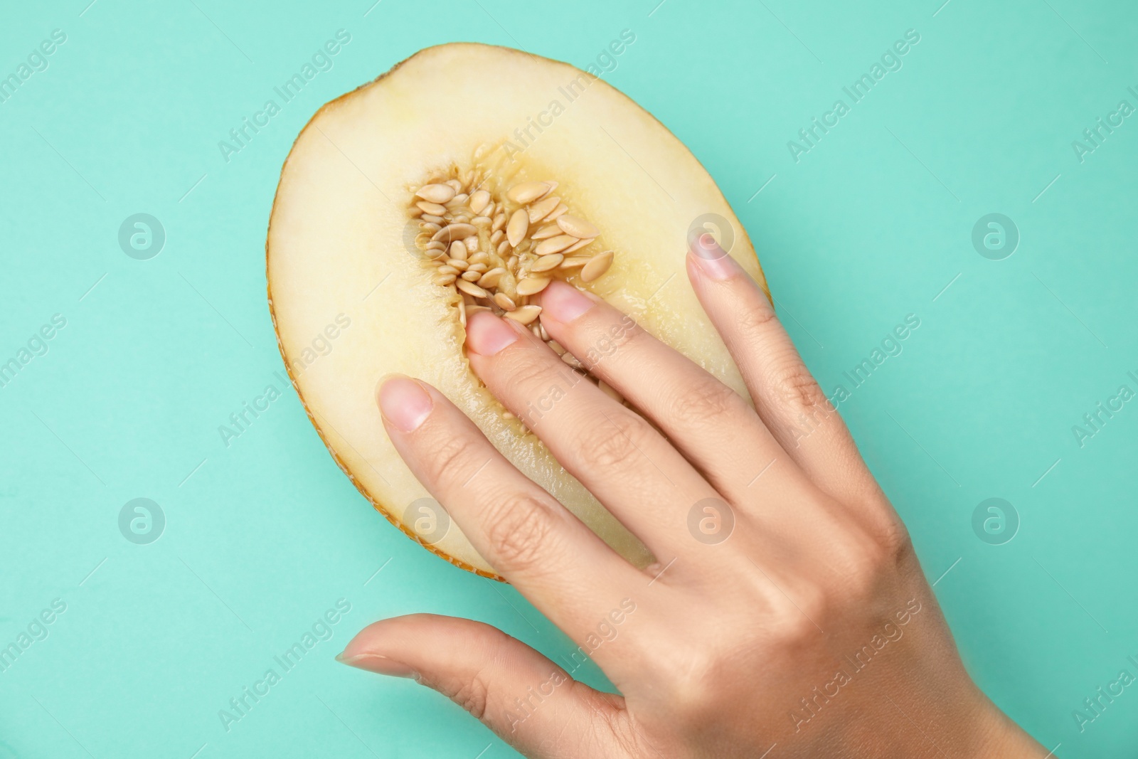 Photo of Young woman touching half of melon on turquoise background, above view. Sex concept