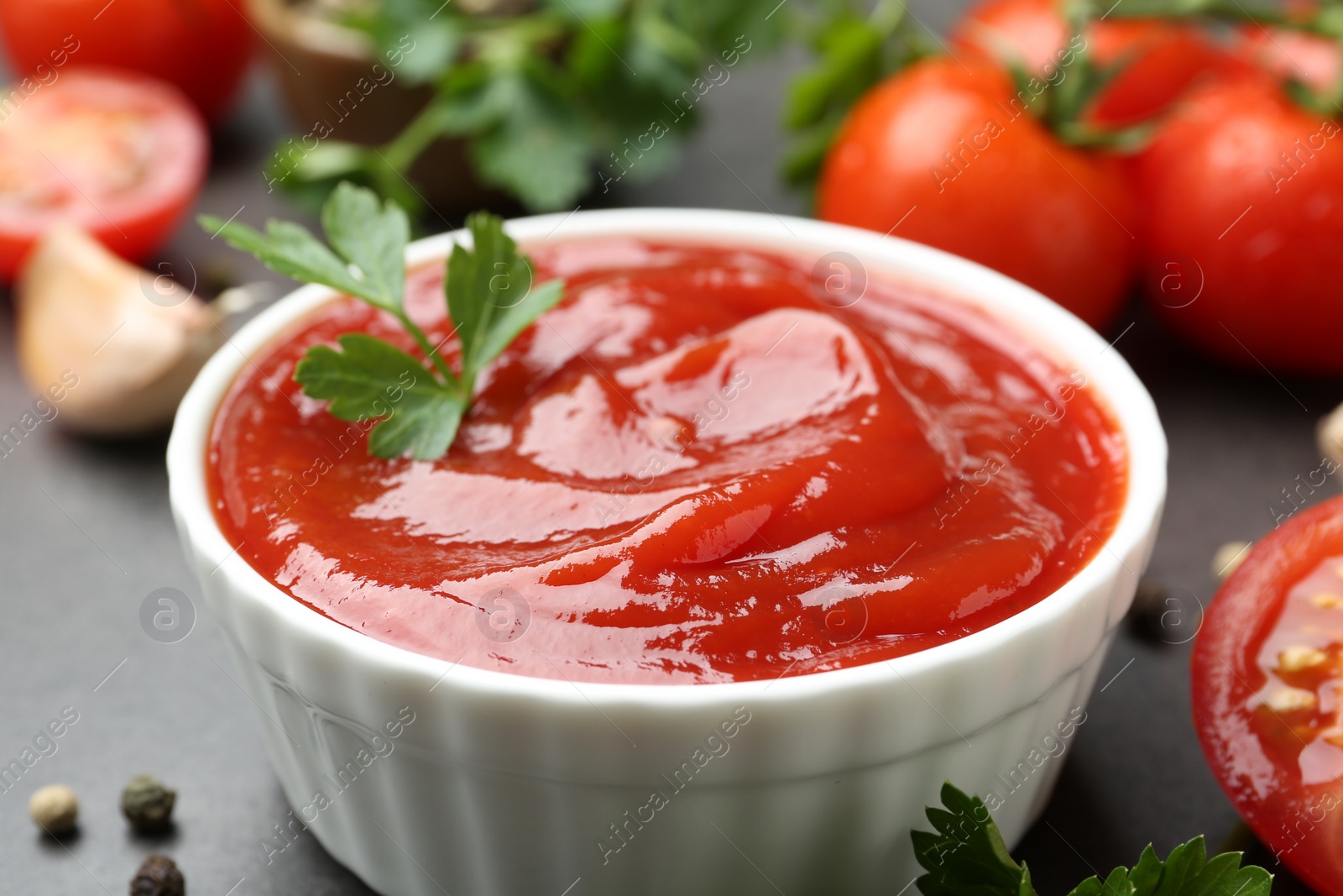 Photo of Delicious tomato ketchup and parsley in bowl on grey table, closeup