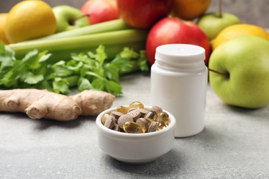 Photo of Dietary supplements. Blank white bottle and different pills in bowl near food products on grey textured table, closeup