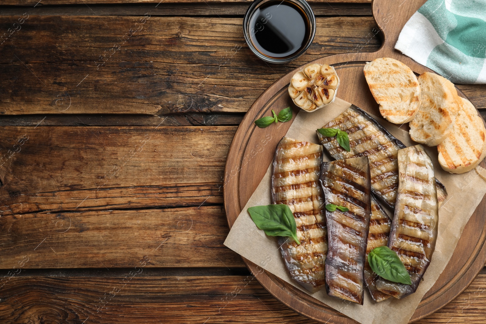 Photo of Delicious grilled eggplant slices served on wooden table, flat lay. Space for text