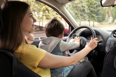 Photo of Mother with little son on knees driving car and talking by phone. Child in danger