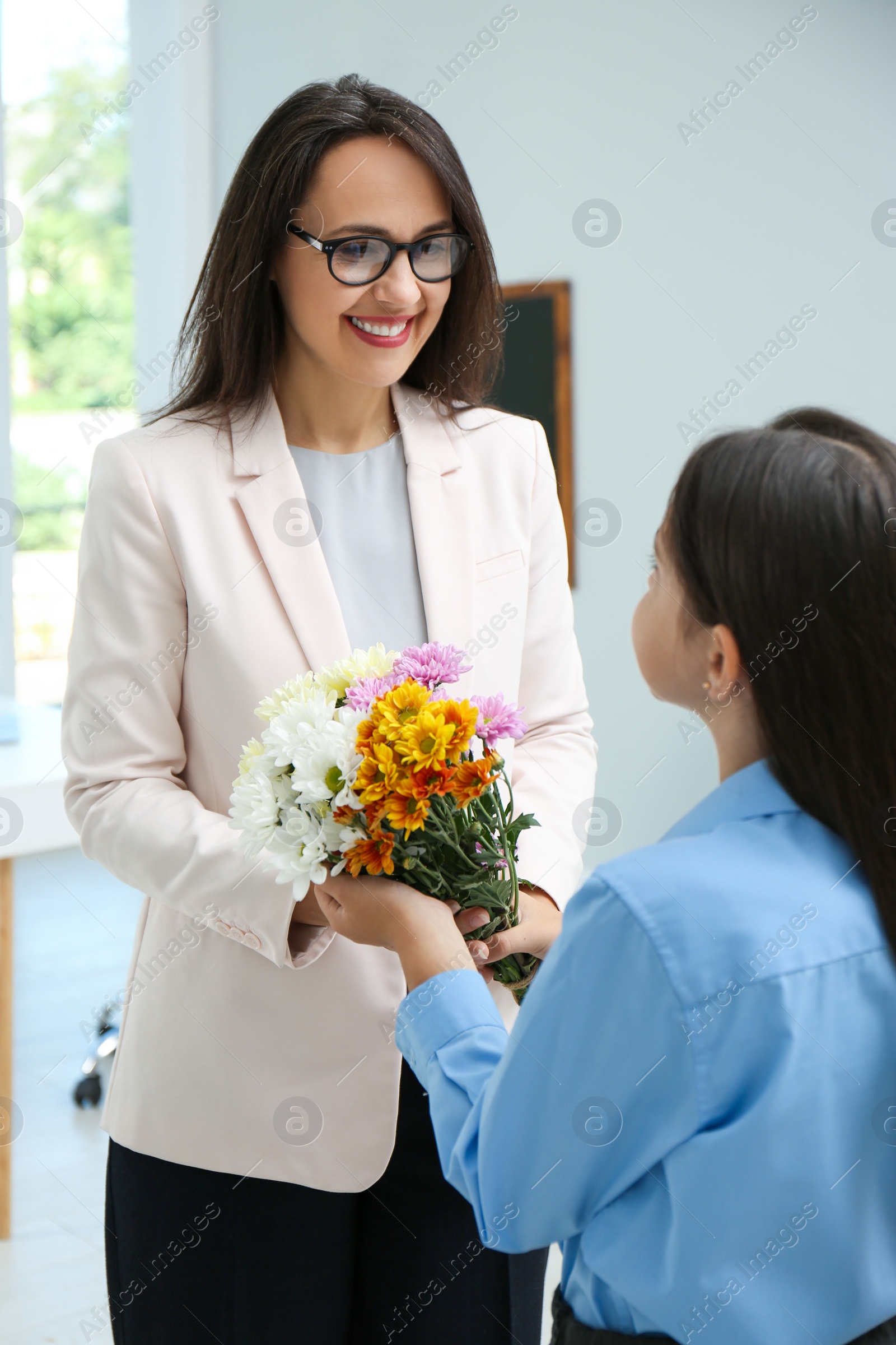 Photo of Schoolgirl congratulating her pedagogue with bouquet in classroom. Teacher's day