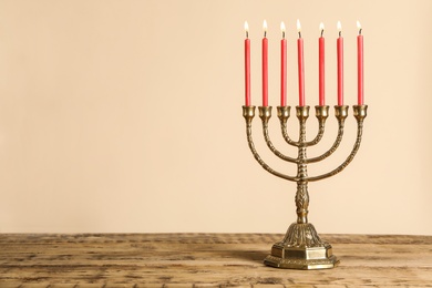 Photo of Golden menorah with burning candles on wooden table against beige background, space for text
