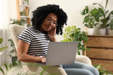 Photo of Relaxing atmosphere. Woman with laptop sitting in armchair surrounded by houseplants at home