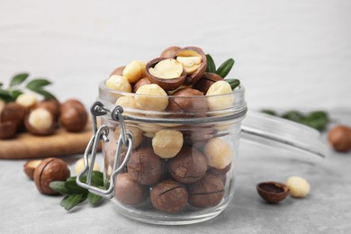 Photo of Tasty Macadamia nuts in jar on light grey table, closeup