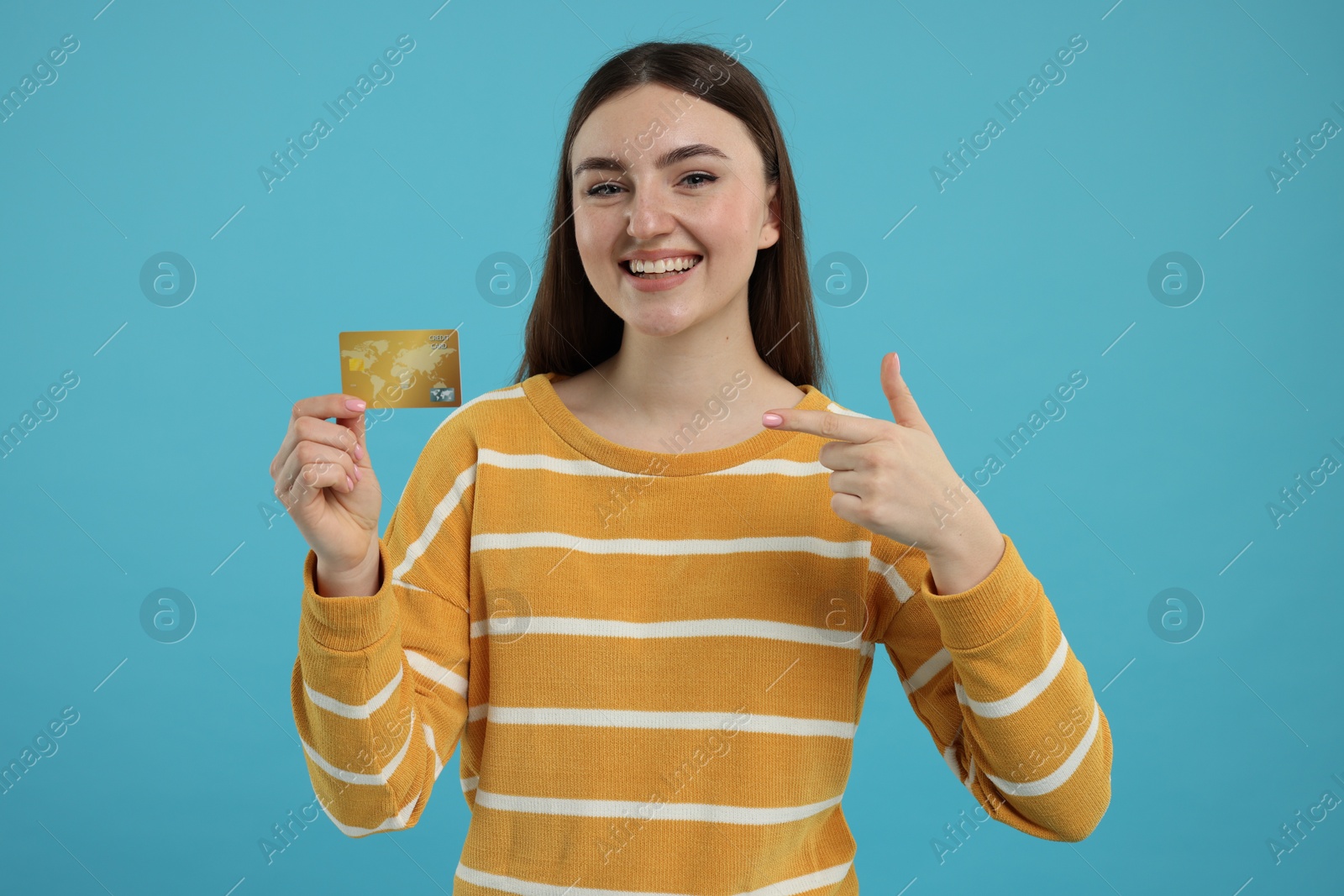 Photo of Happy woman pointing at credit card on light blue background