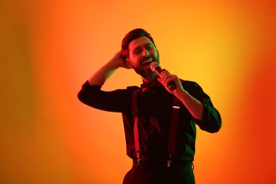 Photo of Emotional man with microphone singing in neon lights on orange background
