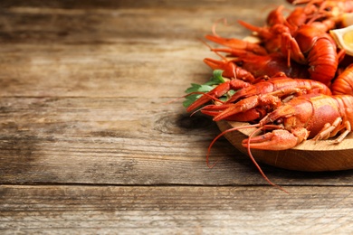 Photo of Delicious boiled crayfishes on wooden table, space for text